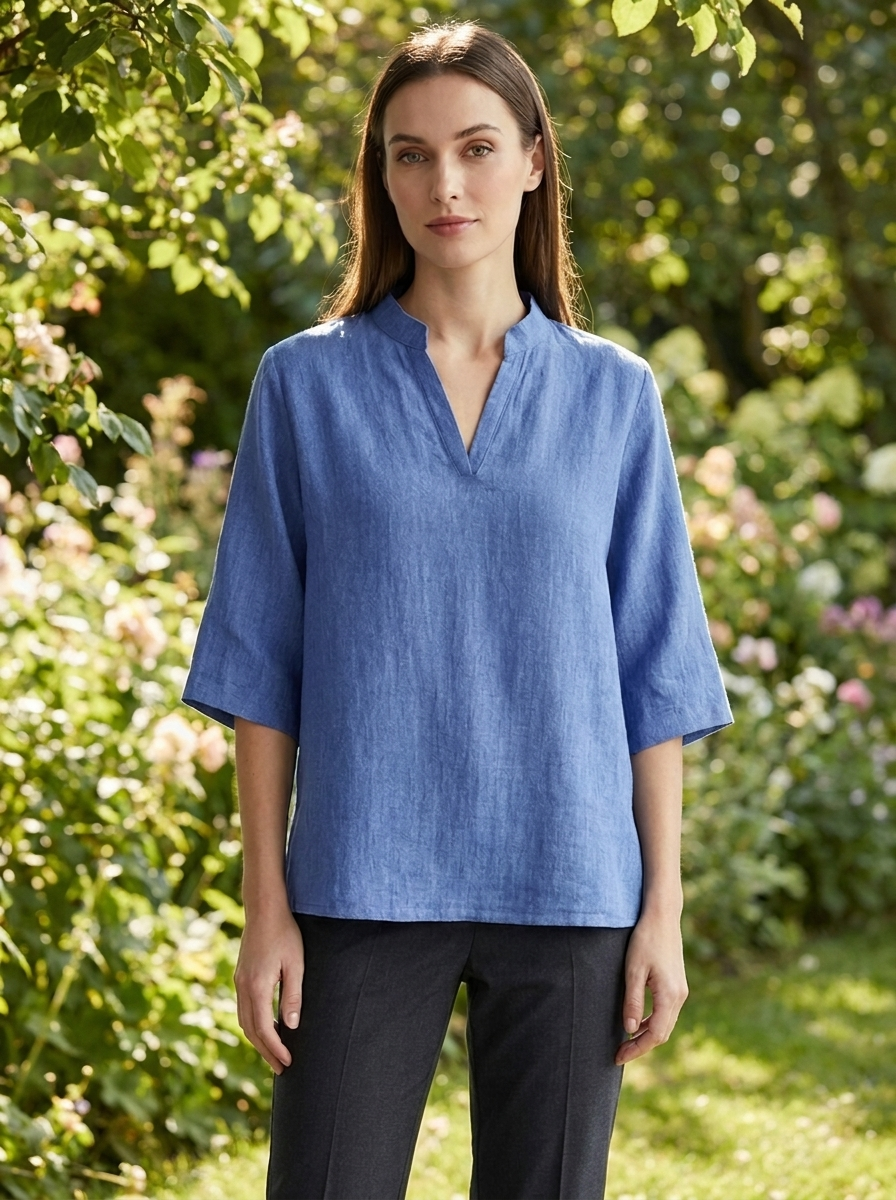 Woman wearing Estelle blue linen tunic blouse in a sunlit summer garden