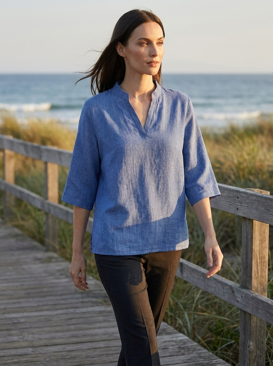 Woman wearing Estelle blue linen tunic blouse on a coastal boardwalk at golden hour
